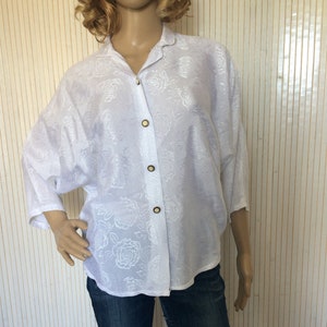 May include: White button-up shirt with a floral pattern. The shirt has a relaxed fit and three-quarter sleeves.