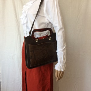 Pode incluir: Uma bolsa de mão de couro marrom com padrão de pele de cobra e uma alça superior de plástico transparente. A bolsa tem um fecho de aba e um pequeno bolso na frente.