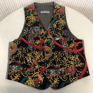 May include: A black waistcoat with a gold and red patterned design. The waistcoat has a V-neck and a button closure. The label "Ted Lapidus" is visible on the inside of the waistcoat.