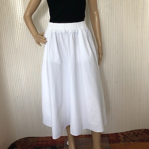 Può includere: Una gonna midi bianca con elastico in vita. La gonna è realizzata in tessuto leggero e ha una silhouette fluida.