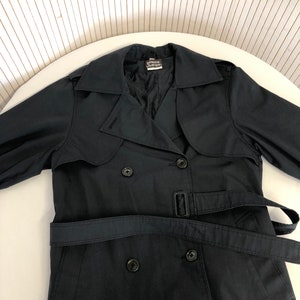 May include: A black double-breasted trench coat with a belt. The coat has a label that reads "Pierre Cardin" on the inside collar.