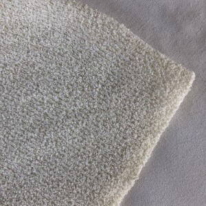 May include: Close-up of a white, textured fabric with a soft, fuzzy appearance. The fabric is slightly wrinkled and has a subtle sheen.