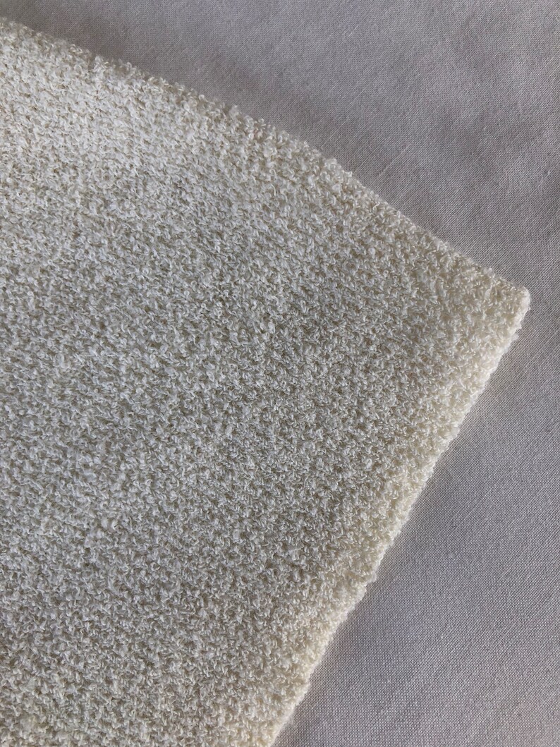 May include: Close-up of a white, textured fabric with a soft, fuzzy appearance. The fabric is slightly wrinkled and has a subtle sheen.