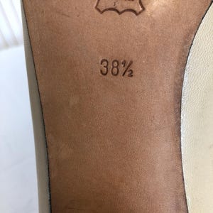 May include: Close-up of a shoe sole, showing a leather surface with the text "CUIR VERITABLE" and the size "38 1/2" embossed. The leather is a light brown colour.