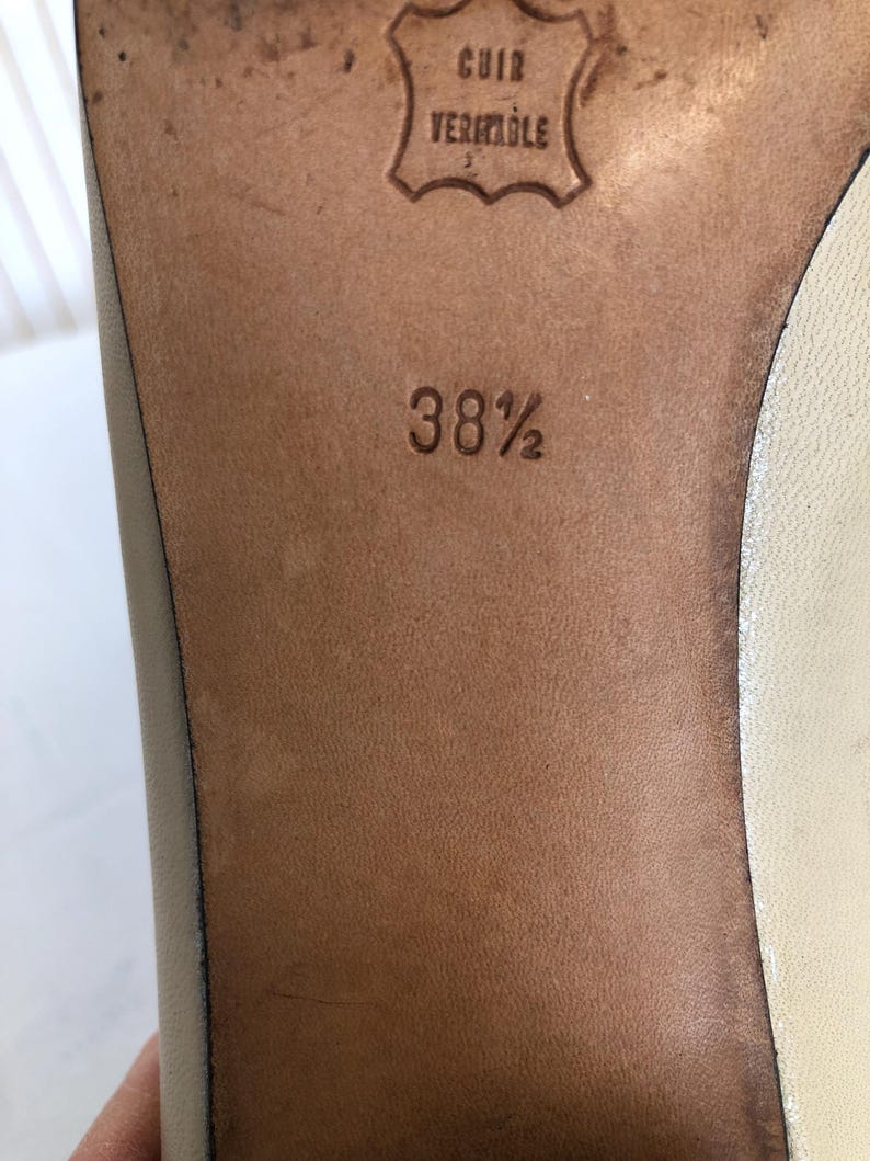 May include: Close-up of a shoe sole, showing a leather surface with the text "CUIR VERITABLE" and the size "38 1/2" embossed. The leather is a light brown colour.
