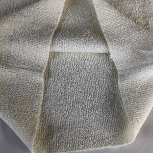 May include: Close-up of a white, textured fabric folded in half. The fabric has a soft, fuzzy texture.