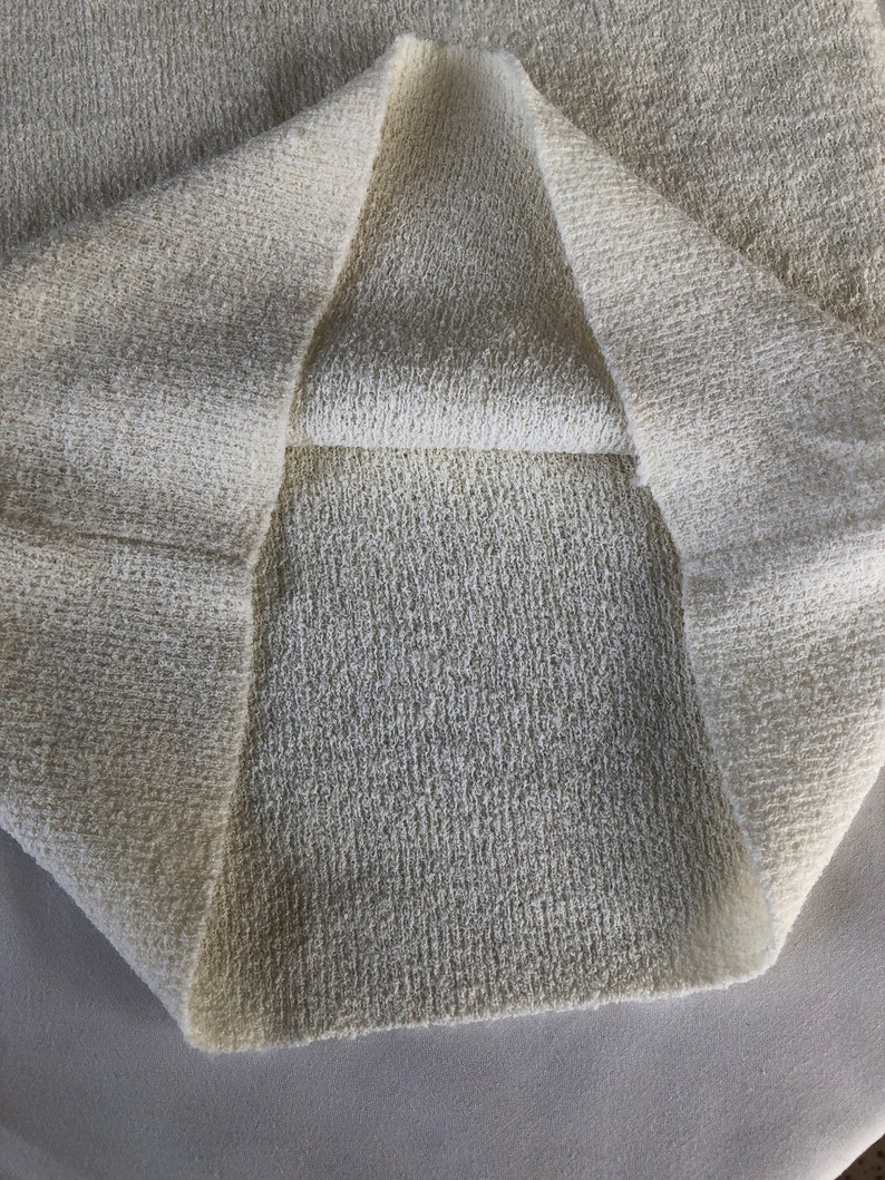 May include: Close-up of a white, textured fabric folded in half. The fabric has a soft, fuzzy texture.