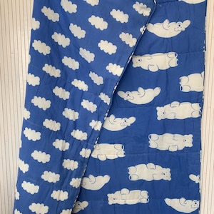 Puede incluir: Una colcha de algodón azul y blanco con un patrón de nubes blancas y osos polares blancos. La colcha está doblada por la mitad, mostrando ambos lados del patrón.