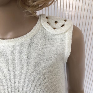 May include: White sleeveless top with a textured knit fabric and gold studs on one shoulder.