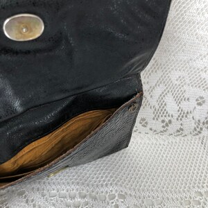 May include: A black leather clutch purse with a gold button closure and a brown fabric lining. The purse is open and the inside is visible.