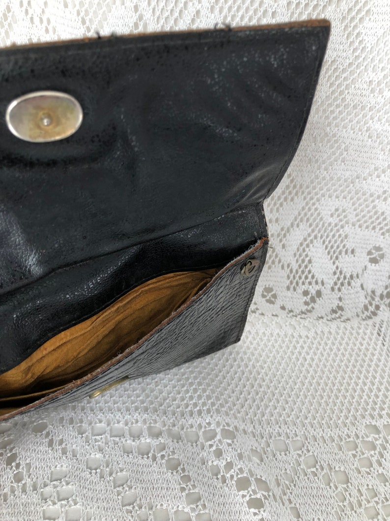 May include: A black leather clutch purse with a gold button closure and a brown fabric lining. The purse is open and the inside is visible.