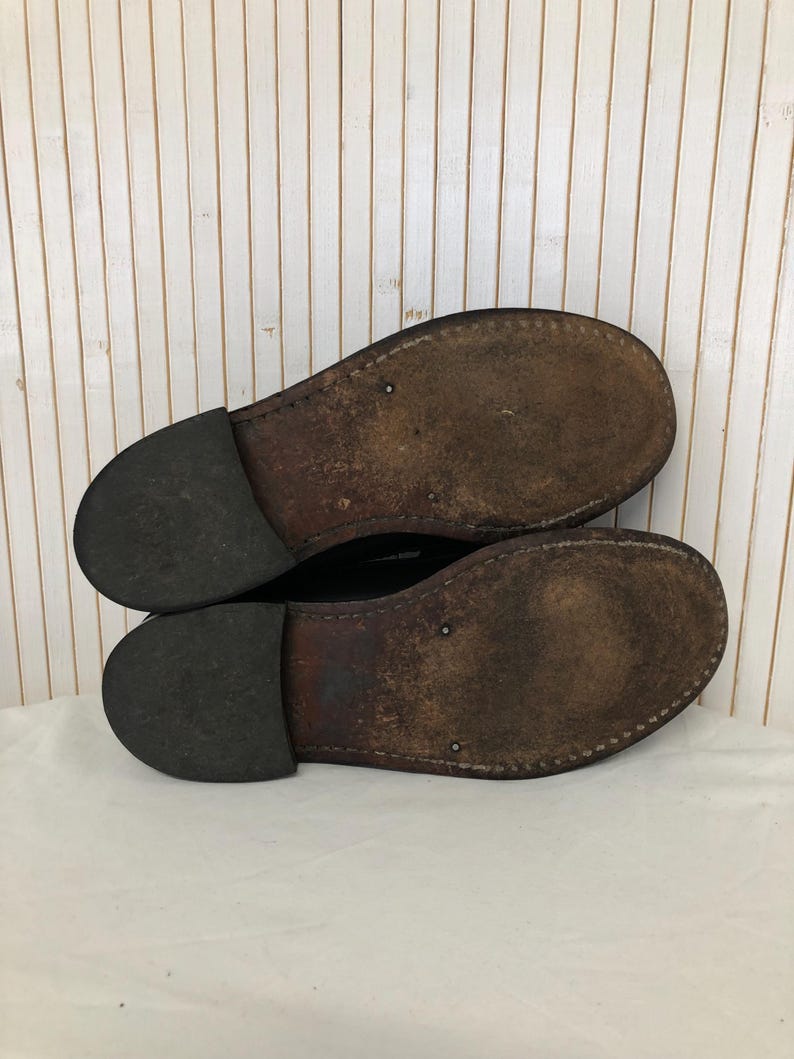 Pu&ograve; includere: Un paio di scarpe in pelle nera con suole in pelle marrone. Le scarpe sono usurate e hanno un aspetto vissuto.