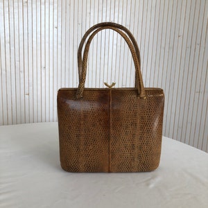 May include: A brown snakeskin handbag with a gold clasp and top handles.