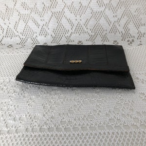 May include: A black leather wallet with a gold clasp. The wallet is closed and lying on a white lace tablecloth.