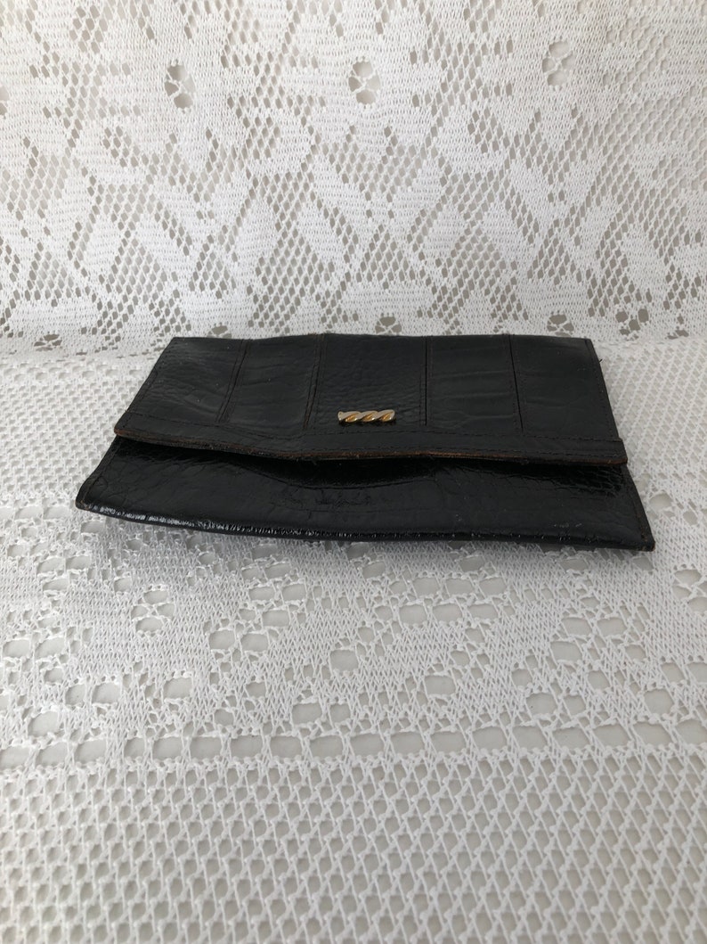 May include: A black leather wallet with a gold clasp. The wallet is closed and lying on a white lace tablecloth.