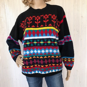 Peut inclure: Un pull noir avec un motif géométrique coloré. Le motif comprend du rouge, du bleu, du vert, du jaune et du blanc. Le pull a des manches longues et un col rond.