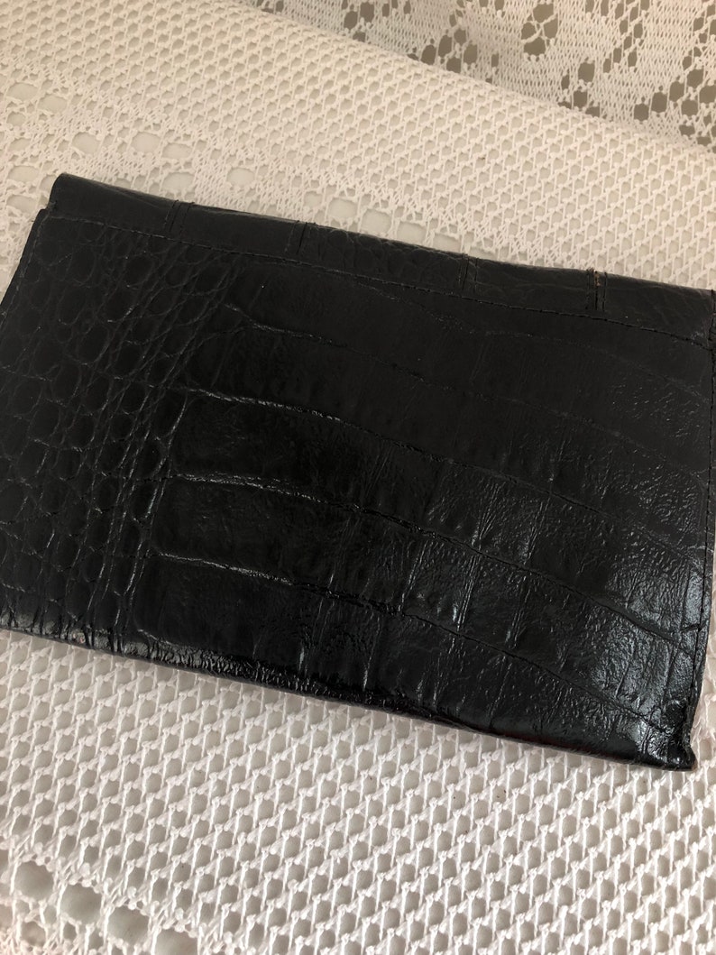 May include: A black leather clutch with a crocodile embossed pattern.