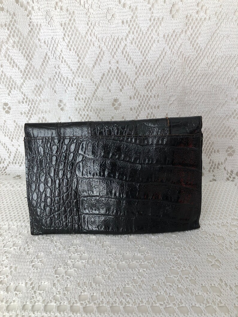 May include: Black crocodile-embossed clutch purse with a flap closure.