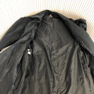 May include: Black trench coat with a smooth lining. The coat is unbuttoned and the lining is visible.