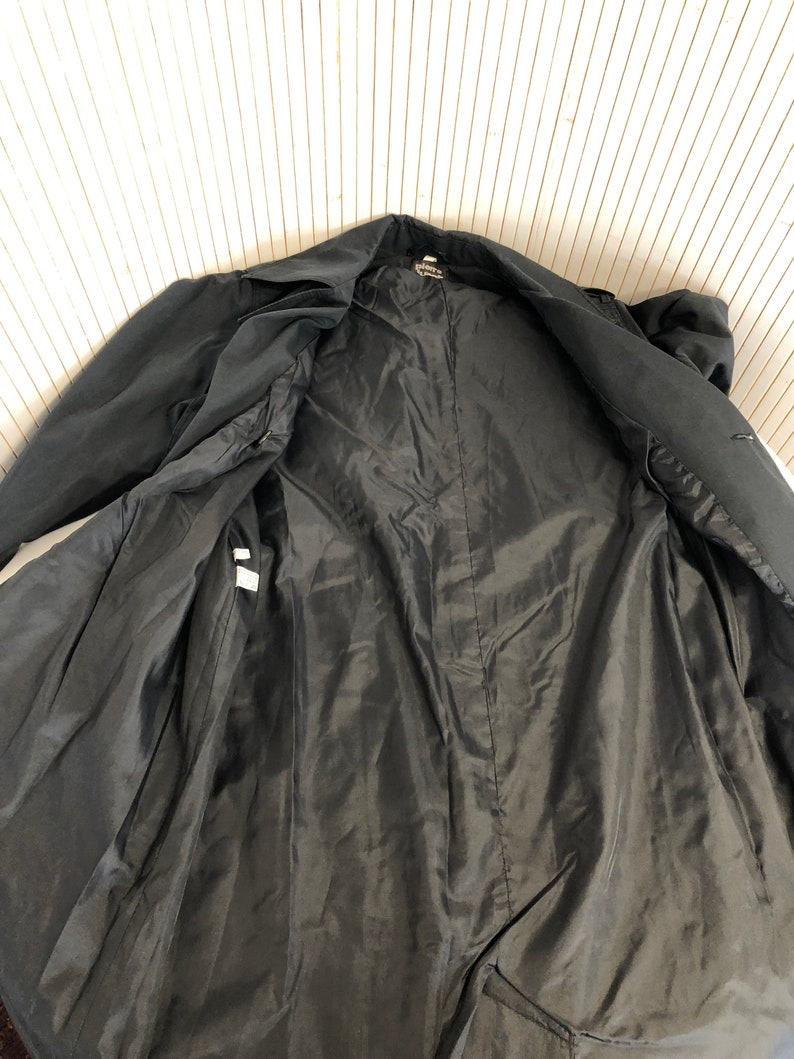 May include: Black trench coat with a smooth lining. The coat is unbuttoned and the lining is visible.
