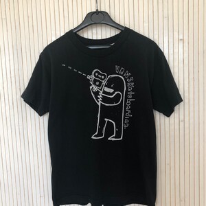 May include: Black t-shirt with a white graphic of a cartoon figure holding a camera and the text "Vans Skateboarding."