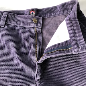 May include: Purple corduroy pants with a zipper and button closure. The pants have a brand label that says "Goon" with a red circle and white outline.