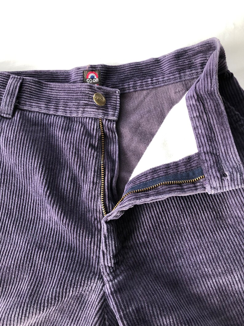 May include: Purple corduroy pants with a zipper and button closure. The pants have a brand label that says "Goon" with a red circle and white outline.