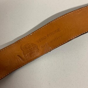 K&ouml;nnte beinhalten: Nahaufnahme des Innenraums eines braunen Lederg&uuml;rtels. Der G&uuml;rtel ist mit "VERO PITONE MADE IN ITALY" und einem Logo versehen. Das Leder hat ein nat&uuml;rliches, strukturiertes Aussehen. Die N&auml;hte sind an den R&auml;ndern sichtbar.