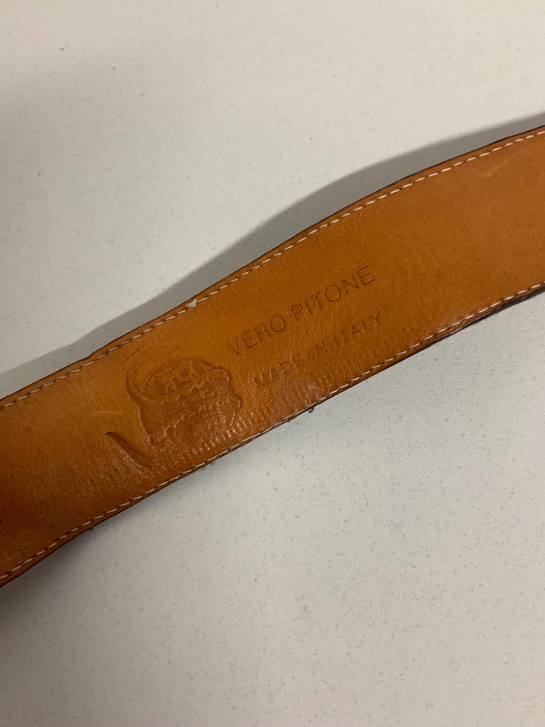 K&ouml;nnte beinhalten: Nahaufnahme des Innenraums eines braunen Lederg&uuml;rtels. Der G&uuml;rtel ist mit "VERO PITONE MADE IN ITALY" und einem Logo versehen. Das Leder hat ein nat&uuml;rliches, strukturiertes Aussehen. Die N&auml;hte sind an den R&auml;ndern sichtbar.