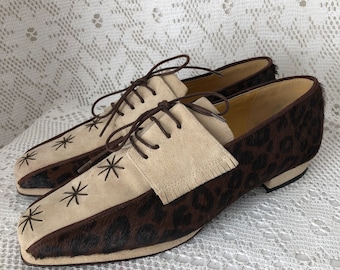 May include: Brown and beige leather shoes with a star pattern on the toe. The shoes have a lace-up closure and a low heel.