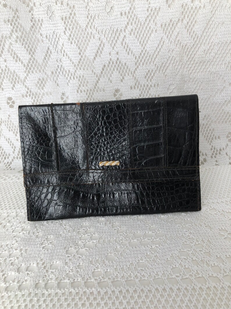 May include: A black leather clutch with a crocodile embossed pattern and a gold clasp.