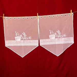 Puede incluir: Dos cortinas blancas de gasa con plantas en maceta bordadas colgando sobre un fondo rojo.