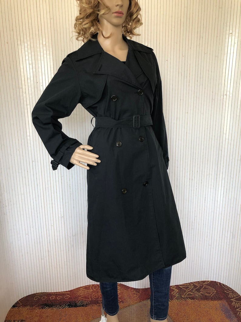 May include: A black double-breasted trench coat with a belt. The coat has a classic design and is made of a smooth fabric.