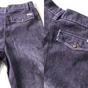 May include: A pair of purple corduroy pants with a patch pocket on the back right side. The pocket has a brown leather flap with a metal button and the word "GOONS" embroidered on it.