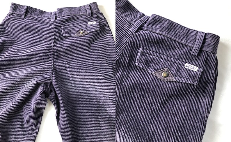 May include: A pair of purple corduroy pants with a patch pocket on the back right side. The pocket has a brown leather flap with a metal button and the word "GOONS" embroidered on it.