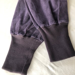 May include: A pair of dark purple corduroy pants with ribbed cuffs. The pants are folded in half and the cuffs are visible.