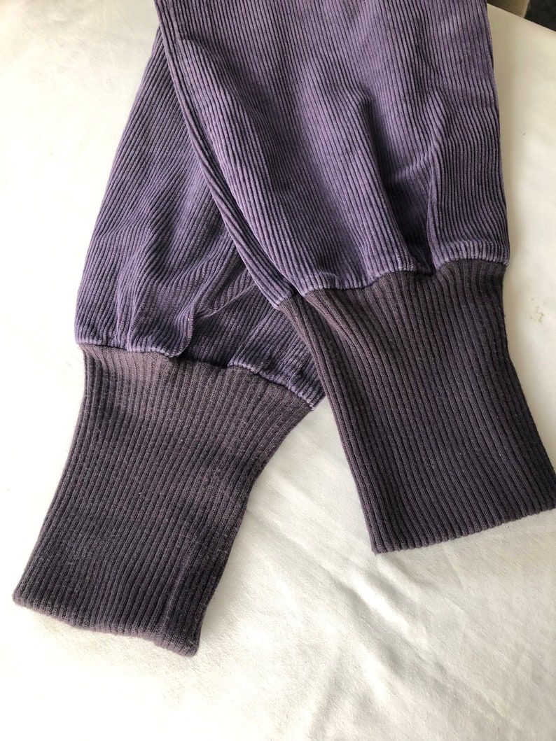 May include: A pair of dark purple corduroy pants with ribbed cuffs. The pants are folded in half and the cuffs are visible.