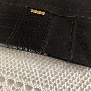 May include: Black leather clutch with a gold clasp. The clutch has a textured surface and appears to be vintage.