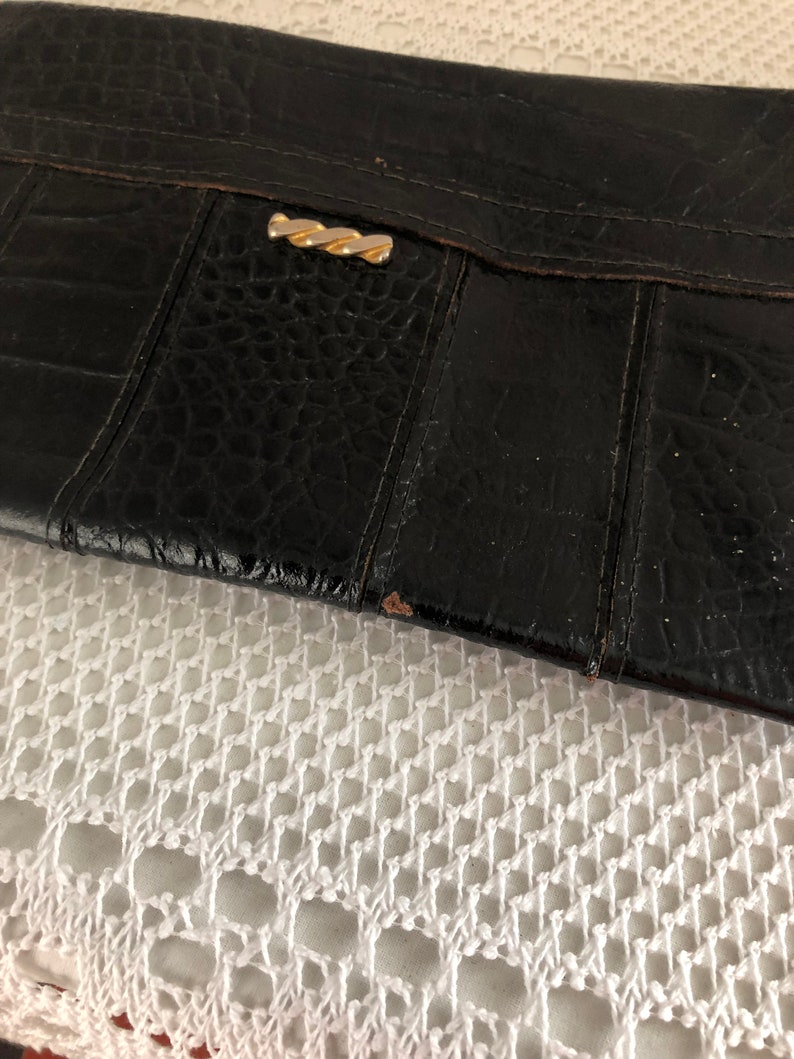 May include: Black leather clutch with a gold clasp. The clutch has a textured surface and appears to be vintage.