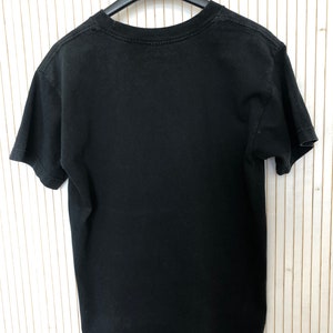 May include: Black short-sleeved t-shirt hanging on a hanger. The t-shirt is plain with no visible graphics or text.