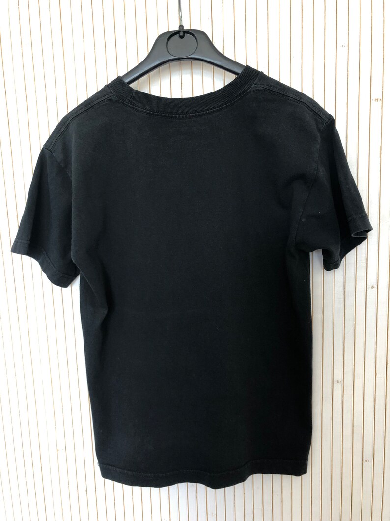 May include: Black short-sleeved t-shirt hanging on a hanger. The t-shirt is plain with no visible graphics or text.