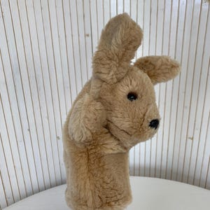 Könnte beinhalten: Eine handgefertigte Hasen-Handpuppe aus beigefarbenem Plüsch. Die Puppe hat lange Ohren, eine kleine schwarze Nase und schwarze Augen. Die Puppe besteht aus weichem, flauschigem Material und ist für die Hand konzipiert.