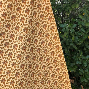 Puede incluir: Una tela de color crema con un patrón repetitivo de motivos florales marrones, verdes y azules. La tela tiene un brillo sutil y una textura suave.