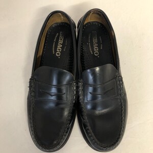 Pu&ograve; includere: Un paio di mocassini Sebago in pelle nera con un dettaglio di cinturino penny. I mocassini hanno un bordo cucito e una soletta interna in pelle marrone con il logo Sebago e "Since 1946" stampato su di essa.