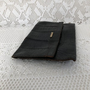 May include: A black leather clutch purse with a textured alligator pattern. The purse has a gold metal clasp.