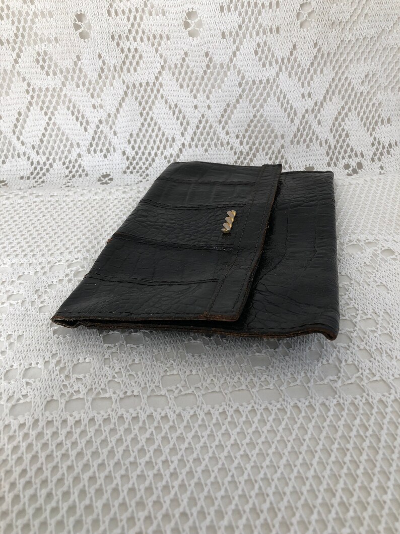 May include: A black leather clutch purse with a textured alligator pattern. The purse has a gold metal clasp.