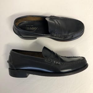Pu&ograve; includere: Un paio di mocassini in pelle nera con un dettaglio di cinturino penny. I mocassini hanno una soletta interna in pelle marrone con il testo "Sebago" e "Since 1946" stampato su di essa.