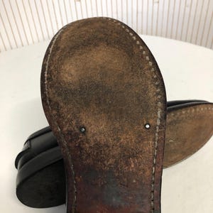 Pu&ograve; includere: Primo piano della suola di un mocassino in pelle nera. La suola &egrave; in pelle marrone con cuciture attorno al bordo. La scarpa ha un aspetto usurato.