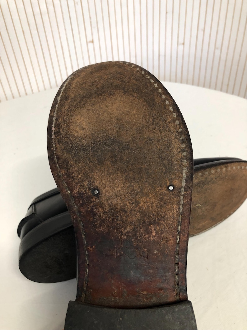 Pu&ograve; includere: Primo piano della suola di un mocassino in pelle nera. La suola &egrave; in pelle marrone con cuciture attorno al bordo. La scarpa ha un aspetto usurato.