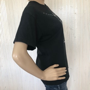 May include: A black short-sleeved t-shirt with a white graphic design. The design features a stylized image of a person with a microphone and a dashed line.